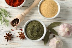 Top view of wooden scoop full of peppercorn with bowls of spice