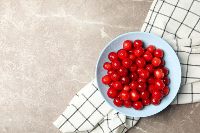Bowl with red cherry and towel on gray background, top view