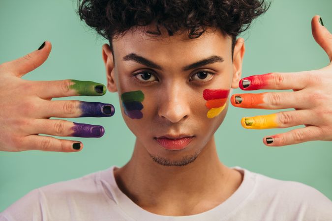 Closeup of a man with rainbow flag colors painted on his face by two hands
