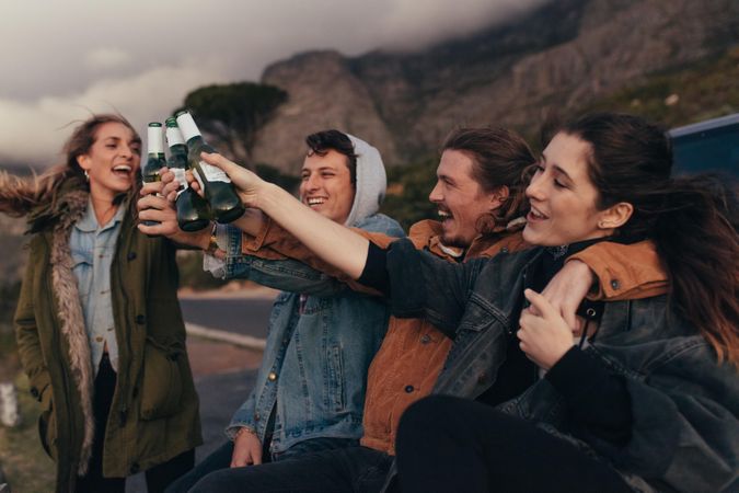 Group of friends sitting on highway toasting bottles of beer