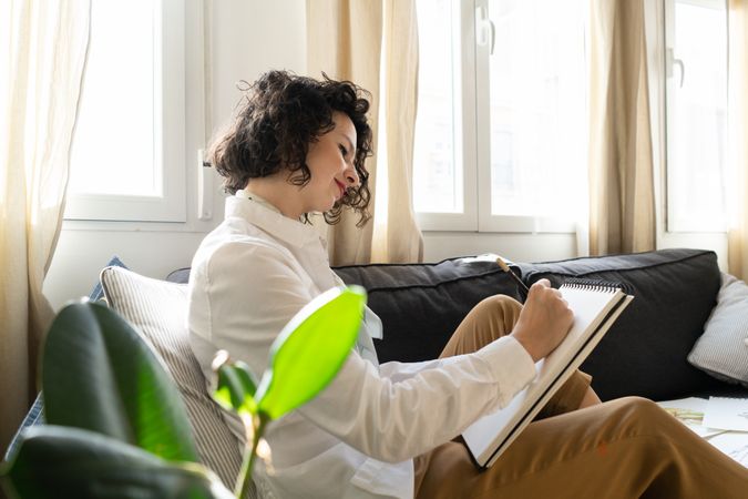 Woman writing on paper on sofa in room