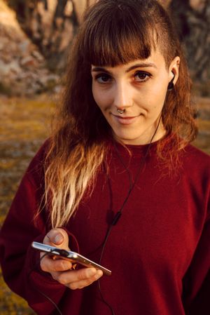 Young woman with piercing listening music on smartphone on hill