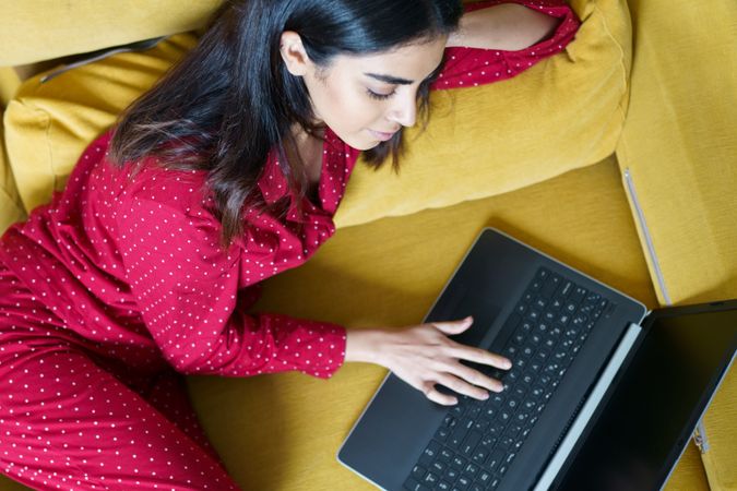 Female relaxing at home using laptop on yellow sofa
