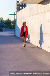 Front view of businesswoman wearing red jacket walking on the street with shadow bGRvLa