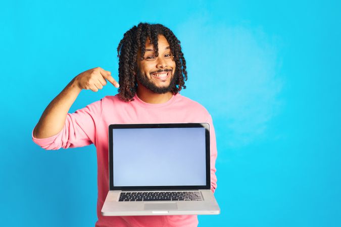 a young man with a happy gesture pointing to the computer isolated on a blue background