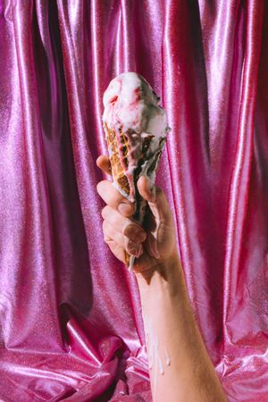 Hand holding melted ice cream on pink curtain background