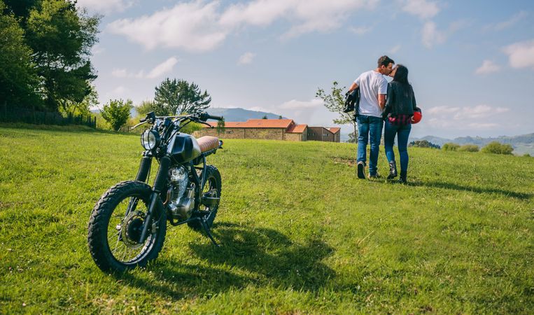 Couple kissing and walking on the field with motorbike