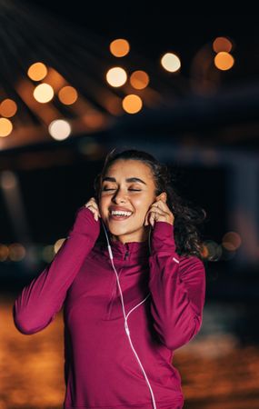 Woman in dark red sport searing smiling while listening to headphones outside