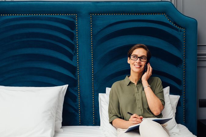 Woman sitting on a bed with a blue headboard taking a phone call