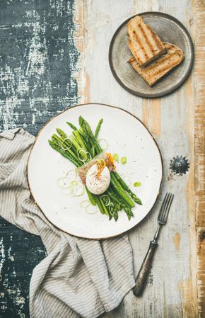 Asparagus and soft boiled egg on plate, on wooden table, with linen, and toast on grey plate