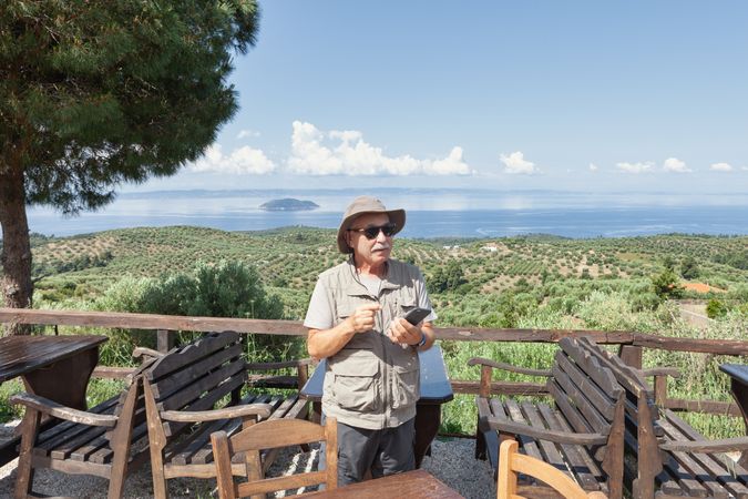 older man with smartphone on terrace with seascape