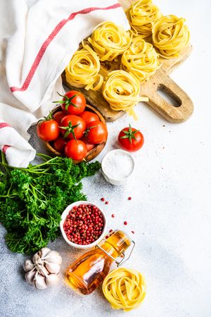 Raw Fettuccine pasta on breadboard surrounded by fresh vegetables