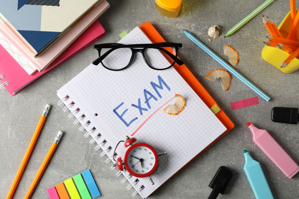 Top view of open notebook with the word “exam” with glasses resting on notebook