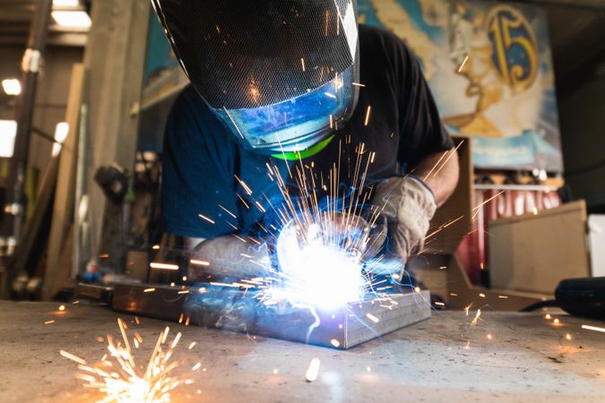 Welder in protective helmet welding metal detail in workshop