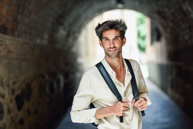 Handsome man standing within arch of city street with backpack