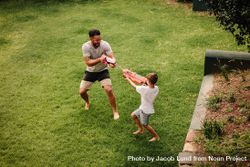 Boy playing water guns with father in backyard lawn 0VKP35