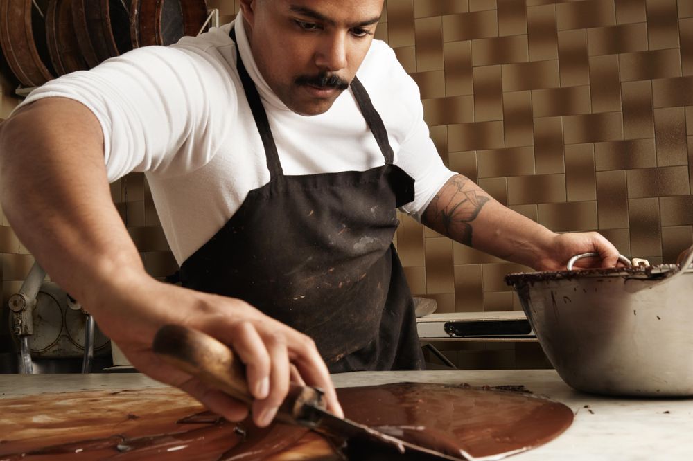 Black male chef working with melted chocolate on marble counter