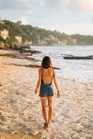 Back of woman in jean shorts and bathing suit walking on Bali beach
