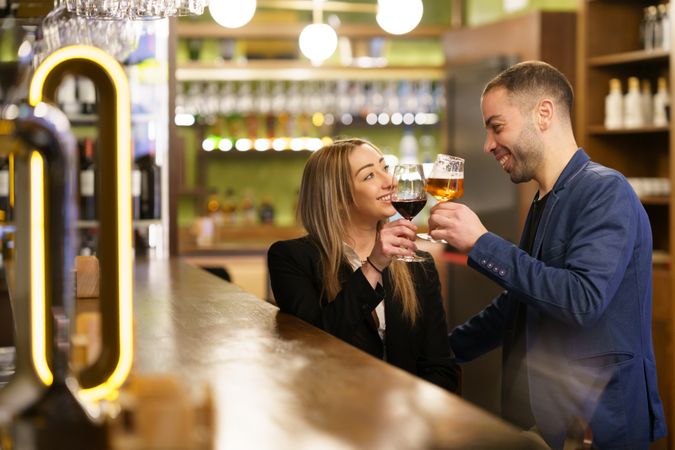 Happy man and woman toasting beer and wine at a bar on date