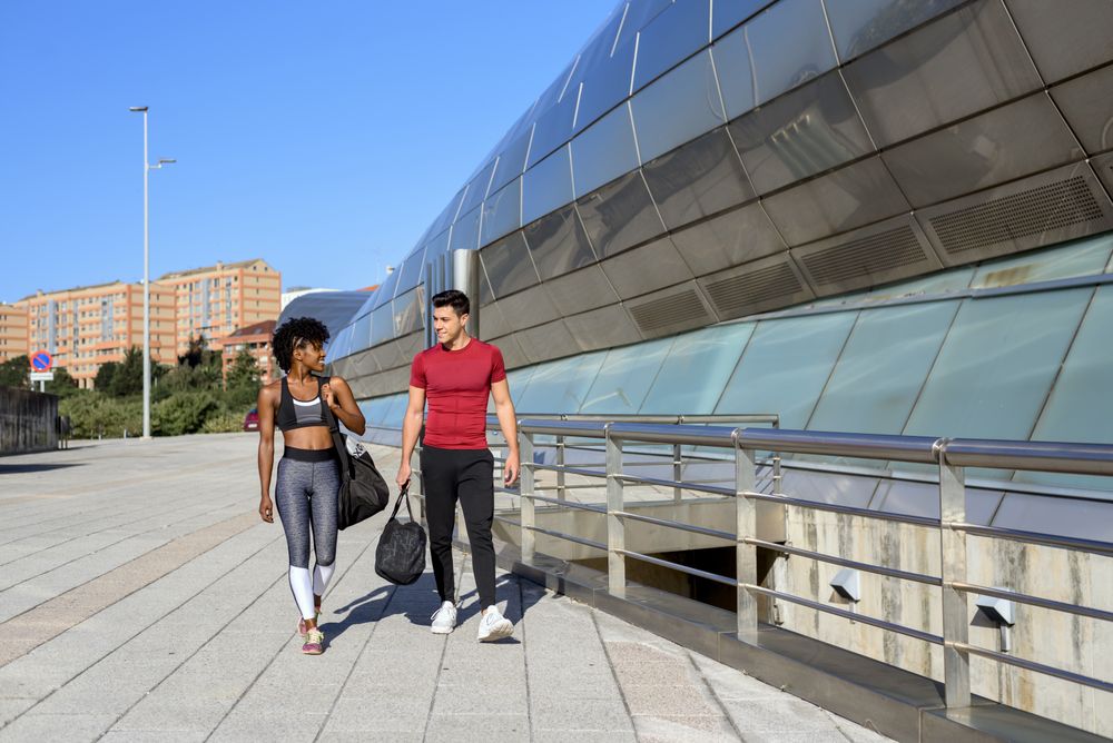 Happy sportive man and woman walking along wall in city