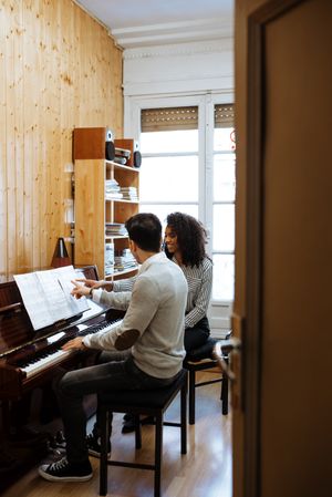 Man playing piano near woman teaching in studio