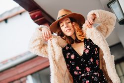 Smiling woman in warm wear standing near building and fence