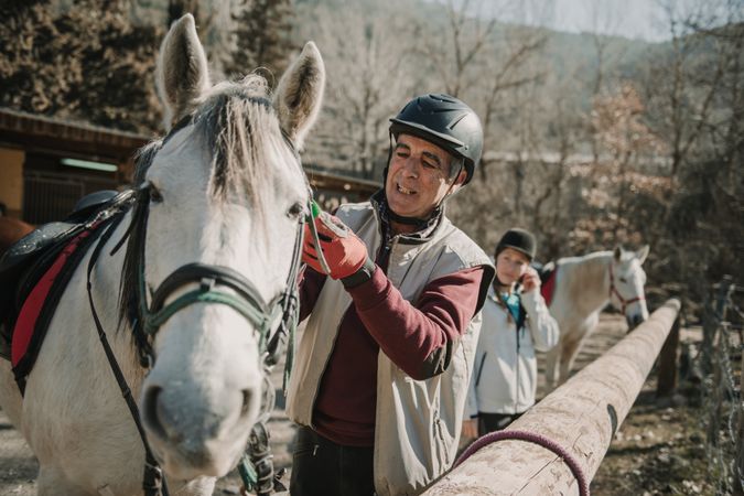 Older man putting bridle on horse