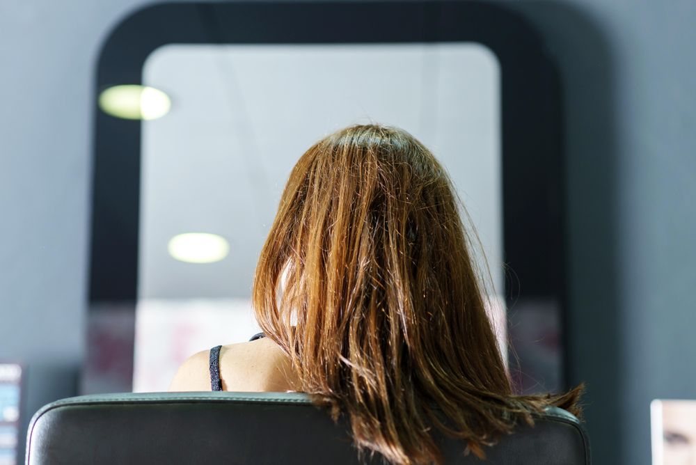 Brunette female sitting in hair stylist’s chair awaiting cut