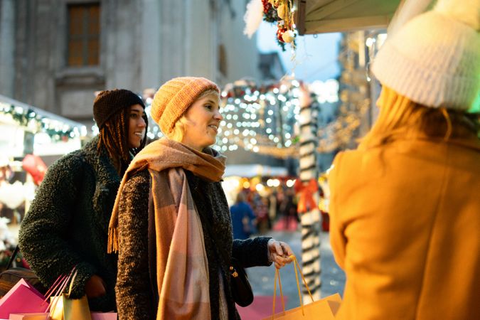 Three friends talking and smiling together at a Christmas market at night.