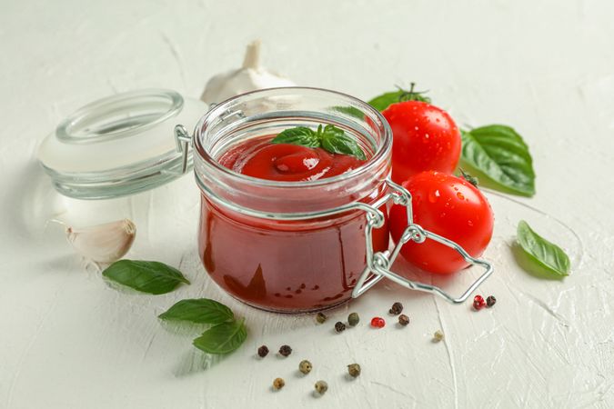 Composition with fresh tomatoes, basil, pepper, garlic and sauce in glass jar on studio background, space for text