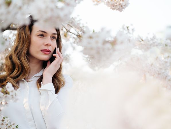 Woman answering phone call near blooming trees