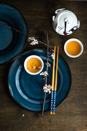Top view of table setting with chop sticks on navy plate and decorative cherry blossom branch and tea pot