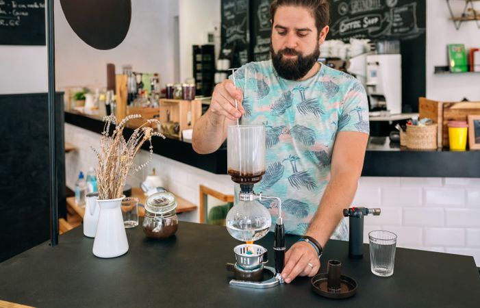Barista skillfully stirring with spoon a specialty coffee into siphon of Japanese coffee maker