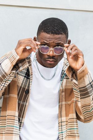 Stylish Black male standing near wall and putting on glasses