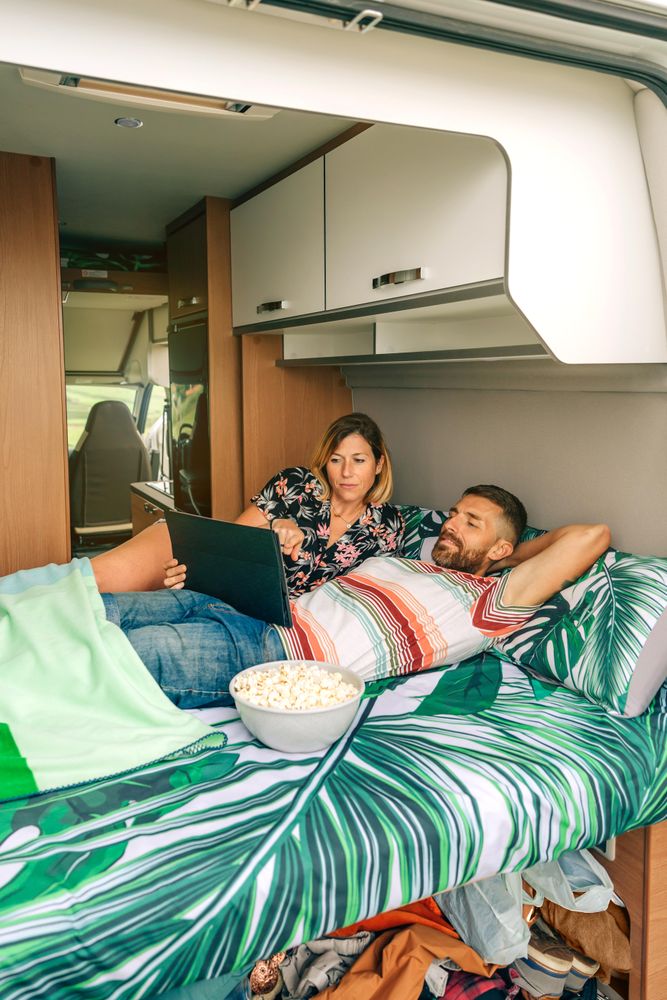 Male and female relaxing on bed in motorhome with popcorn, vertical