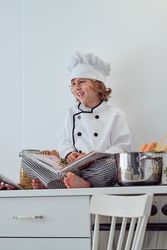 Preteen boy sitting with opened culinary book on kitchen table