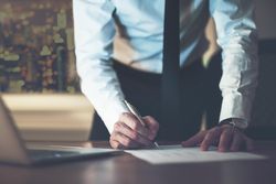 Cropped shot of man in suit and tie writing on paper at desk