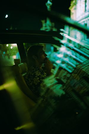 Side view of young man driving an old car and smoking at night