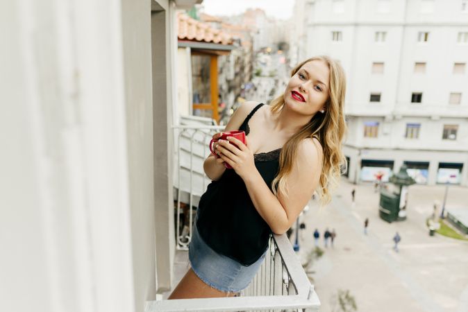 Young cheerful woman holding cup on balcony