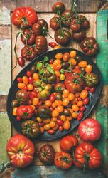 Assortment of different tomatoes in oval bowl, on wooden table, vertical composition