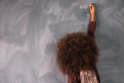 Black girl writing on chalkboard in classroom