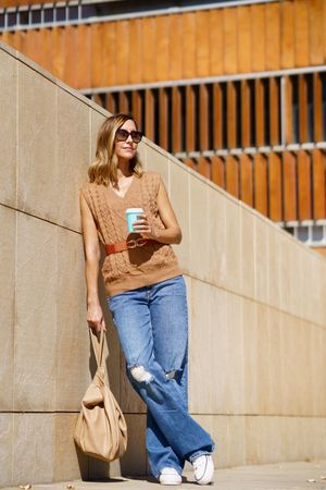 Woman standing in sun with coffee and bag