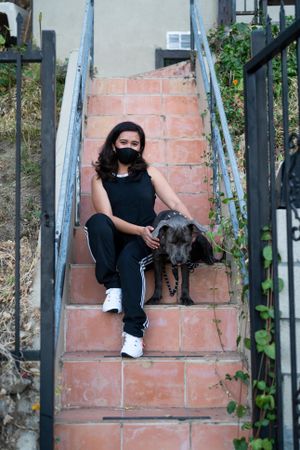 Portrait of woman sitting on steps outside of house wearing athletic casual attire with her pet dog