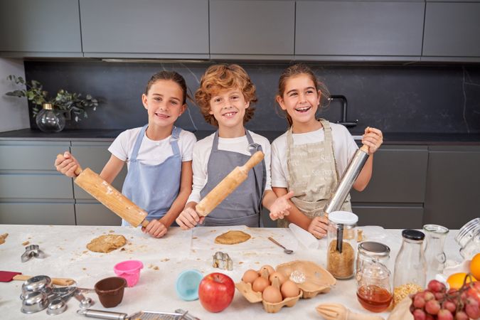Happy children with wooden and metal rolling pins making cookies