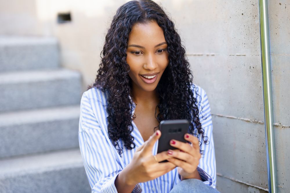 A young woman deeply engaged with her smartphone while sitting on stairs in an urban setting