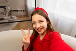 Teen girl taking selfie, smiling and making peace sign.