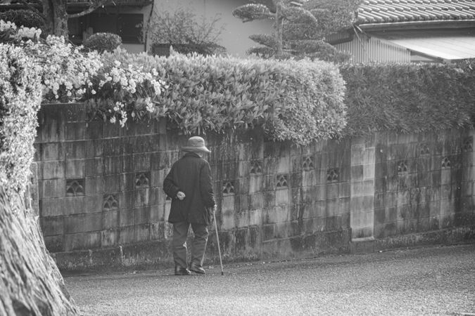 Back view of older man walking beside wall on street in grayscale