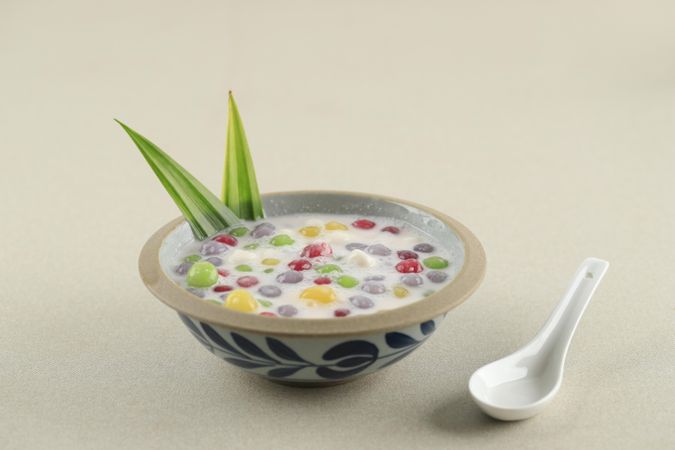 Thai dessert of colorful rice balls in sweet coconut milk on beige table with spoon