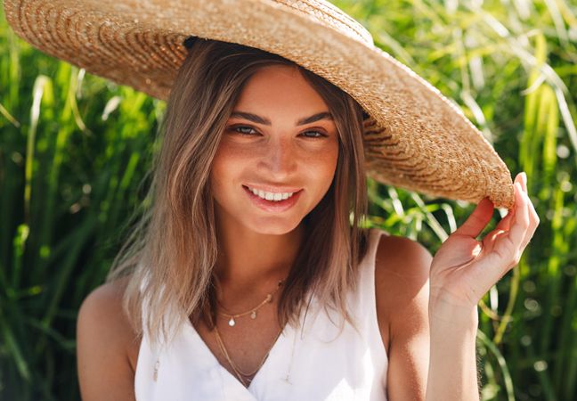 Close up of woman sitting in front of long grass and holding her straw hat