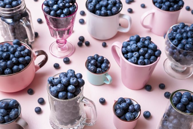 Blueberries in cups, jars and glasses on a pink table